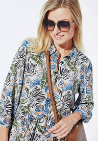 Fließende graue Bluse mit buntem tropischem Blumenmuster in Blau, Orange und Grün. Verfügt über einen Knopfverschluss vorne und Dreiviertelärmel.