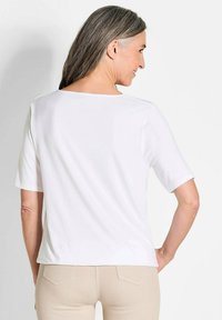 Witte top met korte mouwen en een vierkante halslijn, gladde textuur en een ontspannen pasvorm. Het achteraanzicht laat een lichte drop hem zien, minimalistisch ontwerp.