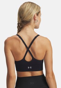 Zwarte sportbeha met een racerback ontwerp, verstelbare schouderbanden en een gestructureerde afwerking met een klein grijs logo op de achterkant.