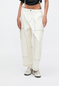 Λευκό, κοντό παντελόνι με αντίθετη μαύρη ραφή, κάθετες τσέπες και χαλαρή γραμμή. Φορεμένο με ελαφριά, υφασμάτινα αθλητικά παπούτσια.