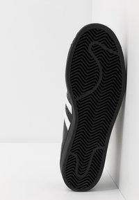 Svart sneaker med en texturerad gummisula, med vita ränder och en slank design. Sidoansiktet framhäver det distinkta mönstret på sulan.