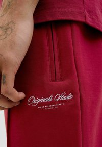 Sweatshirt bordeaux à manches courtes, doté d'une poche cousue et du logo "Originals Studio" brodé en blanc près de l'ourlet.