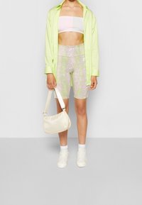 Světle zelená volná košile, pastelově zelený bandeau top, růžovo-zelené vzorované cyklistické kraťasy, krémová taška, bílé tenisky a posádkové ponožky.