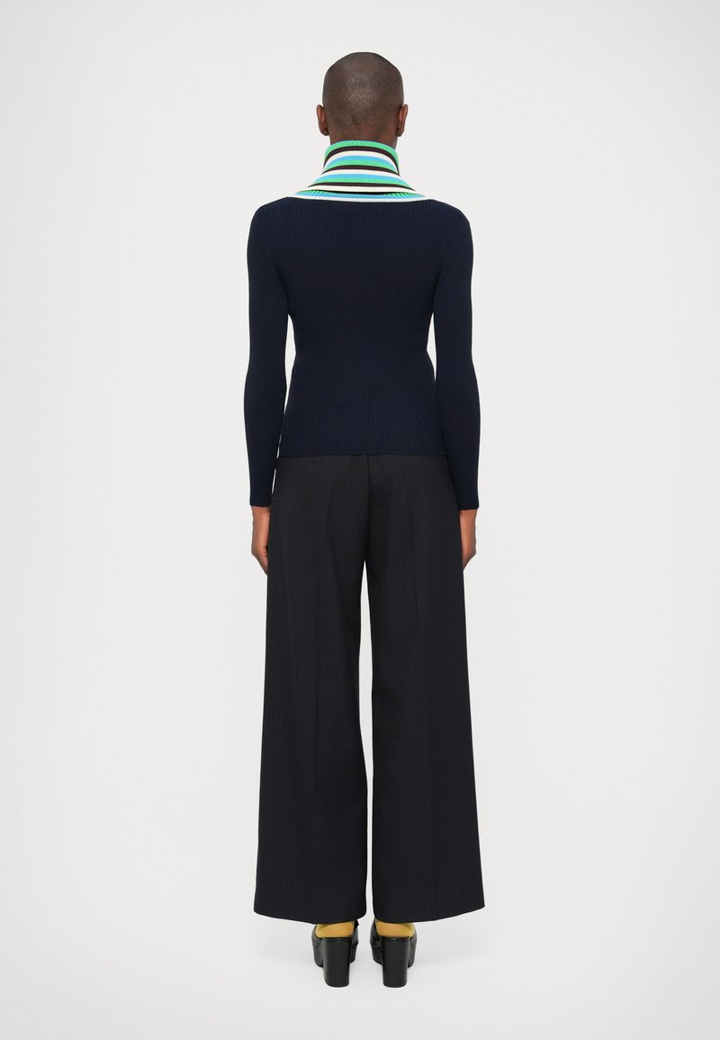 Navy ribbelgebreid top met een gestreepte kraag, gecombineerd met wijd uitlopende zwarte broeken. Kenmerken zijn een aansluitende pasvorm en contrasterende kleur van de kraag.