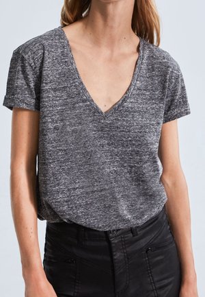 Grijze, kortgerande t-shirt met V-hals ontwerp, gemaakt van een gestructureerde gebreide stof. Gecombineerd met zwarte strakke broek.