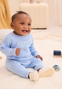 Sada světle modrého pleteného svetru a kalhot s bílými detaily a nápisem "BAKER". K outfitu doplňují boty s měkkou podrážkou.