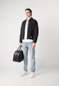 Chaqueta bomber acolchada negra con cierre de cremallera sobre un sudadera blanca, jeans azul claro y zapatillas blancas. Sosteniendo un bolso de cuero negro.