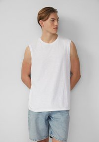 Witte mouwloze T-shirt gemaakt van lichte stof met een relaxte pasvorm, gecombineerd met lichtblauwe denim shorts, eenvoudige ronde halslijn, zonder zichtbare logo's.
