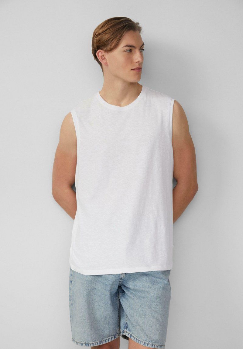 Weißes ärmelloses T-Shirt aus leichtem Stoff mit lockerem Schnitt, kombiniert mit hellblauen Denim-Shorts, schlichter runder Ausschnitt, keine sichtbaren Logos.