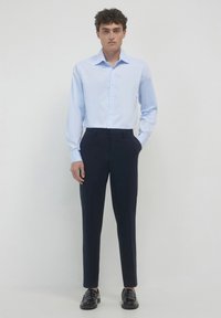 Hellblaues Button-Up-Hemd kombiniert mit dunkelblauen, maßgeschneiderten Hosen. Das Hemd hat einen klassischen Kragen und lange Ärmel. Schwarze Slipper runden den Look ab.