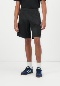 Black athletic shorts with vertical stripes, elastic waistband, and logo detail. Worn with blue shoes and white socks. Simple, functional design.