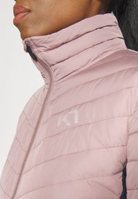 Jasnoróżowa kurtka puchowa z wysokim kołnierzem, poziomymi przeszyciami, przednim zamkiem błyskawicznym i subtelnym logo na piersi. Gładka, miękka w dotyku tekstura.