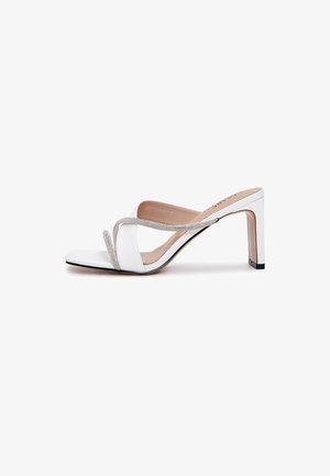 Bijela natikača na visoku petu s kvadratnim vrhom, dva tanka sjajna remena i blok petom, prikazana sa strane na bijeloj pozadini.