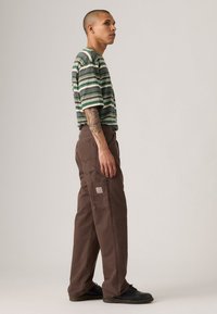 Pantalons de travail marron avec une coupe ample, dotés d'une poche latérale. Le t-shirt à rayures horizontales multicolores a des manches courtes et un design décontracté.