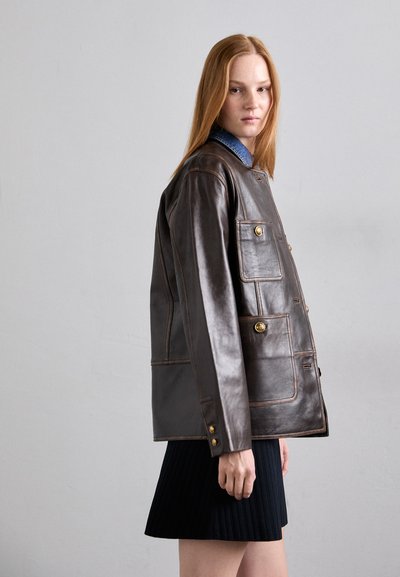 Bruine leren jas met een relaxed fit, voorzien van gouden knopen, patchzakken en een contrasterende blauwe kraag, tegen een neutrale achtergrond.