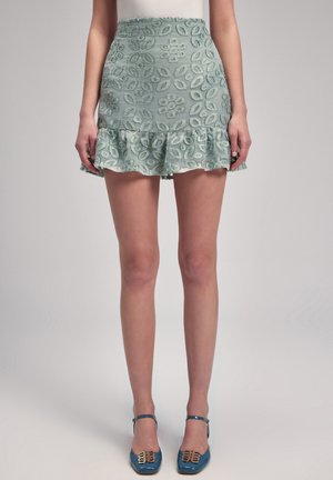 Jupe bleu clair avec broderie florale, ourlet volanté, taille ajustée. Associée à des escarpins bleus avec des accents dorés, créant un look harmonieux.