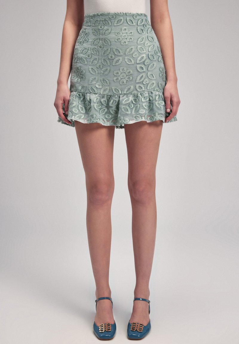 Falda azul claro con bordado floral, dobladillo con volantes, cintura ajustada. Combinada con tacones azules con acentos dorados, creando un look coherente.