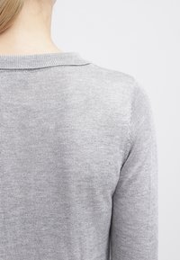 Maglione grigio lavorato a maglia con una texture morbida, dotato di un collo arrotondato e design semplice. La foto mostra la vista posteriore, evidenziando l'area del collo.