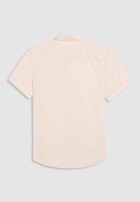 Camisa de manga corta en rosa claro, confeccionada con algodón suave, con un dobladillo recto, detalle en la espalda y una textura sutil.