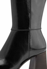 Black leather ankle boot with visible stitching and a thick wooden block heel.
