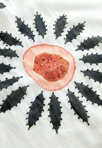 Tissu blanc avec un motif circulaire de formes de feuilles noires entourant un centre pêche orné de petites perles et de paillettes.