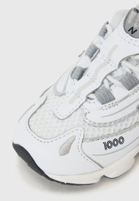 White athletic shoe featuring a mesh upper with gray accents, a padded tongue, and rubber sole, marked with "1000" on the side.