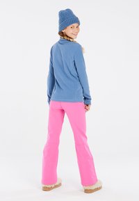 Blauwe fleecejas, roze broek en een gebreide blauwe muts. De broek heeft een flared ontwerp met fleece-gevoerde manchetten en een gladde textuur.