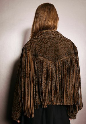 Person mit langem Haar trägt eine braune Jacke mit Leopardenmuster, die lange Fransen und sternförmige Nieten am oberen Rücken aufweist.