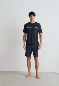 Set de îmbrăcăminte sport de culoare gri închis, compus dintr-un tricou cu mânecă scurtă cu o dunga orizontală albă și pantaloni scurți asortați, realizat dintr-un material moale și ușor.