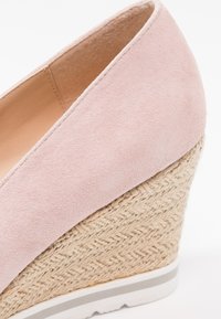 Escarpin en suède rose avec un talon en jute tressé. La semelle est dotée d'une base en caoutchouc blanc avec une bande grise en accent.