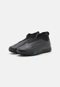 Schwarze Sportschuhe mit einer strukturierten Oberseite, elastischer Knöchelstütze und einem grünen Akzent auf der Außensohle, mit einem typischen Logo-Detail.