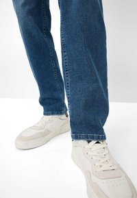 Jeans in denim blu con taglio dritto, abbinati a sneakers bianche e beige con tomaia testurizzata e lacci a vista.
