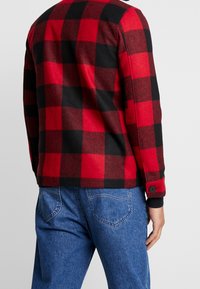 Rød- og sortternet flannel skjorte, lange ærmer, rundet kant, knapmanchetter, stofteksten er blød og varm, stylet med blå denim jeans.