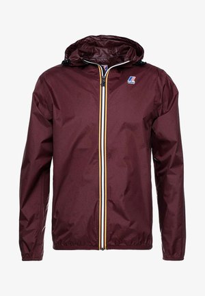 Veste de pluie à capuche couleur marron rouge, avec poignets élastiques, fermeture éclair frontale avec des rayures jaunes, blanches et bleu marine, et logo K-Way sur la poitrine.