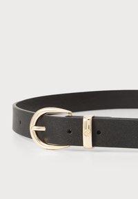 Ceinture en cuir noir avec une texture lisse, dotée d'une boucle en métal doré et d'un design simple. La boucle a une forme arrondie et une fermeture sécurisée.