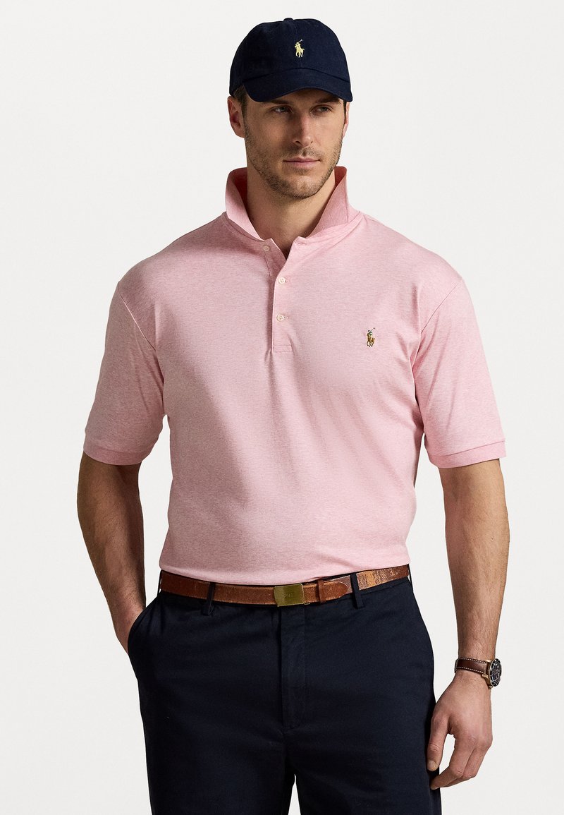Tricou polo roz deschis, cu mânecă scurtă, guler cu buton și un logo mic. Purtați-l cu pantaloni negri și o curea maro, completat de o șapcă bleumarin.