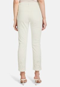 Białe dżinsy mają detale z oczkami przy nogawkach z misternymi wycięciami, prezentując prosty krój nogawki i pięć kieszeni.