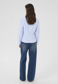 Blå og hvide stribet skjorte med knapper, lange ærmer, skræddersyet pasform og rygstykke-detalje, kombineret med højtaljede, vidde-ben denimjeans.