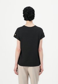 Svart kortärmad T-shirt med rullade ärmslut, rund halsringning och subtila sidsömmar. Slät textur, lättviktig tyg.