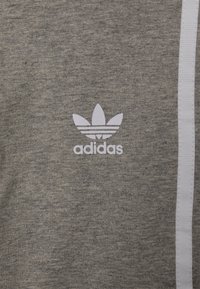 Felpa grigia realizzata in tessuto testurizzato, con logo Adidas bianco e una striscia laterale bianca. Design semplice senza ulteriori motivi.