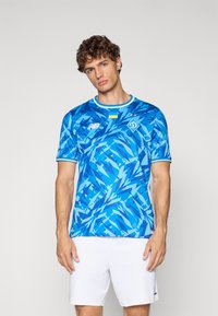 Camisola de futebol de manga curta azul com um padrão abstrato em várias tonalidades de azul, com um colarinho canelado e detalhes de logótipo.
