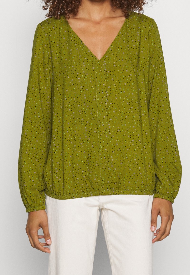 Blusa verde con estampado, con escote en V, mangas largas y puños elásticos. Presenta pequeños diseños en forma de estrella en varios colores. Corte relajado.