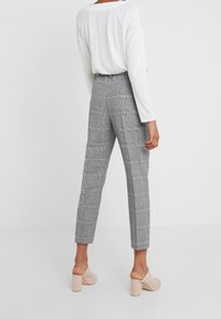 Grijze geruite broek met een getailleerde pasvorm, hoge taille en lengte tot de enkels, gecombineerd met een witte lange mouwen top en beige blockhak schoenen.