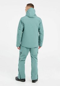 Hemelsblauwe waterdichte jas met capuchon, gecombineerd met bijpassende broek. Voorzien van ritszakken en een relaxte pasvorm. Textuurstof, lichtgewicht ontwerp.