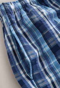Tissu à carreaux bleu et blanc avec taille élastique et coutures visibles sur les poches latérales en coton léger.