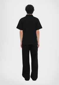 Svart t-skjorte med korte ermer og vide bukser, begge i et ensfarget, matt stoff; avslappet passform; minimal detailing og sømmer synlige på baksiden.