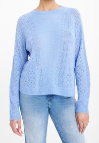 Ljusblått stickat tröja med ett texturerat mönster, som har långa ärmar och ribbad nederkant, ihop med ljusblå denimjeans.