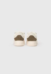 Et par beige og olivengrøn ruskinds sneakers vist fra bagsiden på en ensfarvet lys grå baggrund.