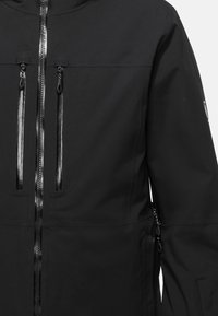 Black jacket featuring a front zipper with two vertical zippered pockets, subtle texture, and a fitted design. No visible logos.