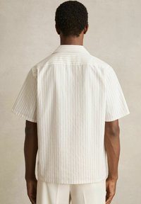 Cămașă cu mânecă scurtă, albă, cu dungi verticale discrete, material texturat, guler ascuțit și tiv drept. Vedere din spate.